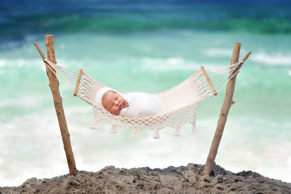 a baby laying in a hammock on the beach