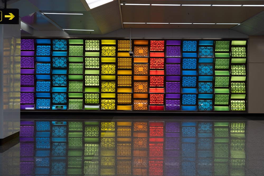 a multicolored wall in an airport with a reflection on the floor