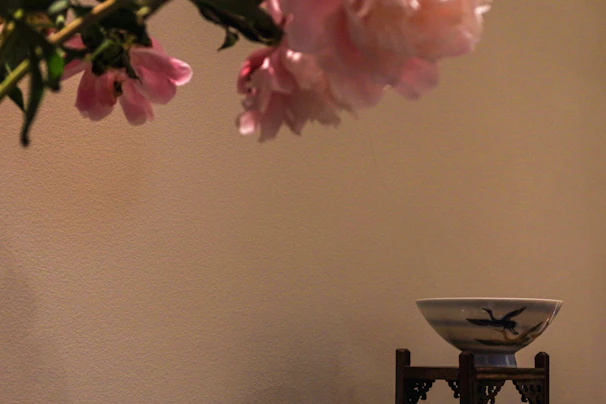 Small decorative display stand holding a delicate ceramic vase, set against a soft cream backdrop.