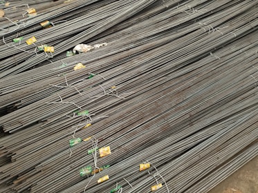 A large stack of steel rebar rods is neatly arranged, with labels and wires securing them at intervals. The rods have a ribbed texture and are uniformly aligned, extending diagonally from one corner of the image to the other.