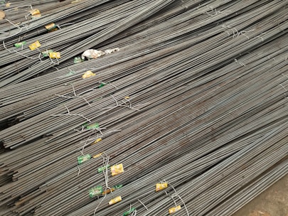 A large stack of steel rebar rods is neatly arranged, with labels and wires securing them at intervals. The rods have a ribbed texture and are uniformly aligned, extending diagonally from one corner of the image to the other.