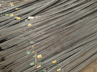 A large stack of steel rebar rods is neatly arranged, with labels and wires securing them at intervals. The rods have a ribbed texture and are uniformly aligned, extending diagonally from one corner of the image to the other.