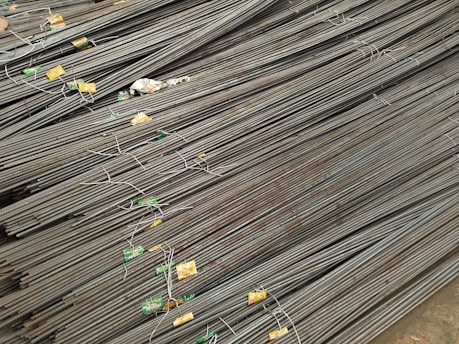 A large stack of steel rebar rods is neatly arranged, with labels and wires securing them at intervals. The rods have a ribbed texture and are uniformly aligned, extending diagonally from one corner of the image to the other.