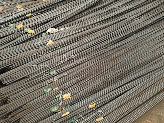 A large stack of steel rebar rods is neatly arranged, with labels and wires securing them at intervals. The rods have a ribbed texture and are uniformly aligned, extending diagonally from one corner of the image to the other.
