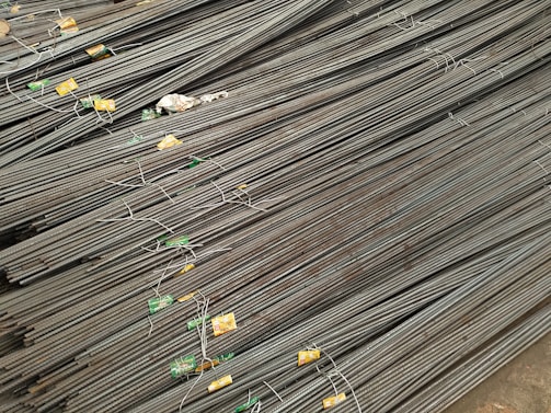 A large stack of steel rebar rods is neatly arranged, with labels and wires securing them at intervals. The rods have a ribbed texture and are uniformly aligned, extending diagonally from one corner of the image to the other.