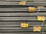 A stack of steel rebars neatly arranged with yellow labels attached to several bars. The labels contain various specifications and certifications. The rebars have a textured surface, indicating they are designed for reinforced concrete use.