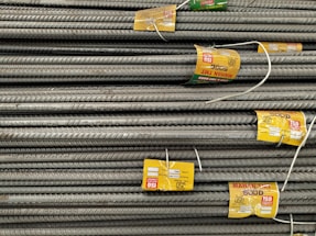 A stack of steel rebars neatly arranged with yellow labels attached to several bars. The labels contain various specifications and certifications. The rebars have a textured surface, indicating they are designed for reinforced concrete use.