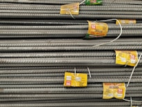 A stack of steel rebars neatly arranged with yellow labels attached to several bars. The labels contain various specifications and certifications. The rebars have a textured surface, indicating they are designed for reinforced concrete use.