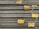 A stack of steel rebars neatly arranged with yellow labels attached to several bars. The labels contain various specifications and certifications. The rebars have a textured surface, indicating they are designed for reinforced concrete use.