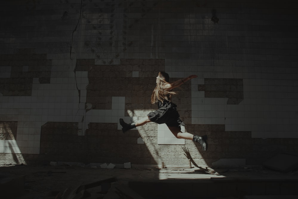 a girl jumping in the air in front of a brick wall