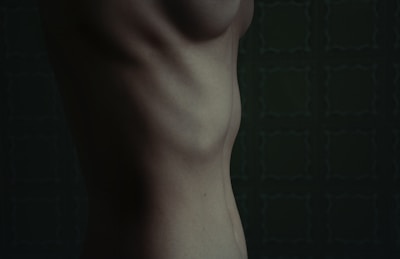 A close-up of a human torso viewed from the side, showcasing the contours of the ribcage and abdomen against a dark, patterned background.