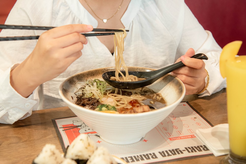 a woman eating a bowl of noodles with chopsticks