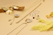 A collection of gold and silver jewelry is displayed on a light beige surface, including necklaces, rings, and earrings. A decorative gold bow and dried yellow flowers add a stylish touch to the arrangement, creating a luxurious and elegant aesthetic.