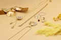 A collection of gold and silver jewelry is displayed on a light beige surface, including necklaces, rings, and earrings. A decorative gold bow and dried yellow flowers add a stylish touch to the arrangement, creating a luxurious and elegant aesthetic.