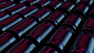 Rows of metal cans are arranged in a tight, orderly pattern. The lighting casts a combination of blue and purple hues on the surface of the cans, creating a futuristic and industrial atmosphere.