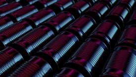 Rows of metal cans are arranged in a tight, orderly pattern. The lighting casts a combination of blue and purple hues on the surface of the cans, creating a futuristic and industrial atmosphere.