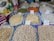Various grains and legumes are displayed in open sacks, each labeled with a price tag. Items include chickpeas, lentils, beans, and other dry goods. There are also cleaning supplies and paper towels in the background.