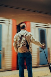 a man with a backpack and a suitcase waiting for a train