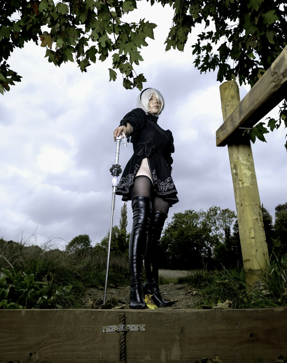 a woman in a black outfit and boots standing on a wooden platform