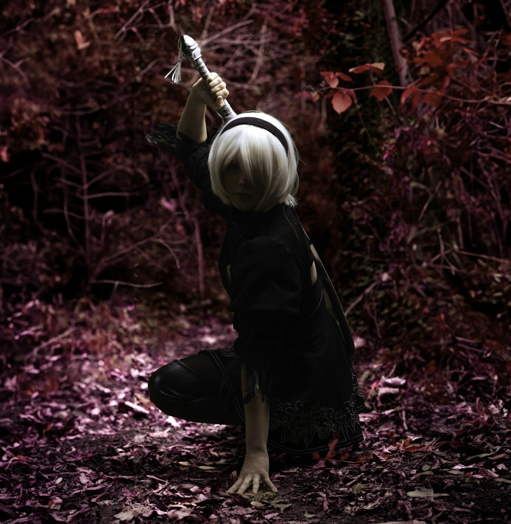 a woman kneeling down in a forest holding a sword
