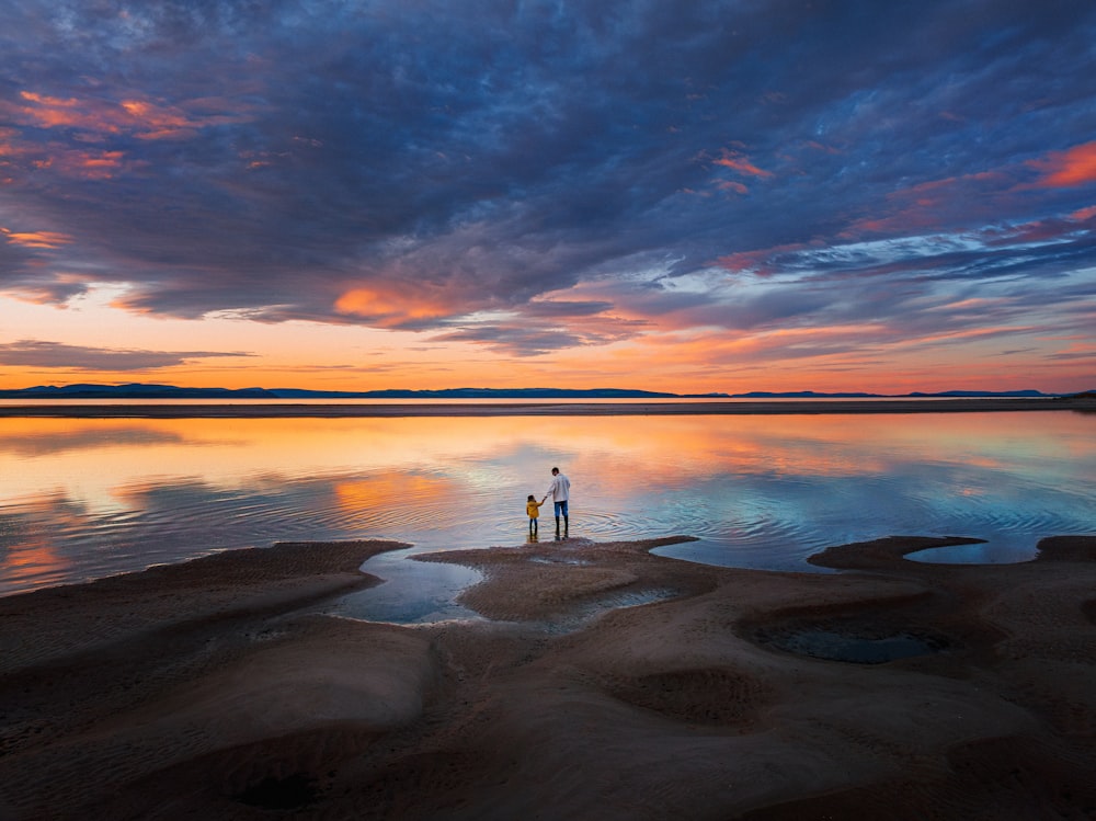 two people standing in the water at sunset