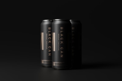 Three sleek, matte black cans are arranged with minimal lighting that highlights their metallic texture and bold typography. The lettering reads 'Black Can' and 'Mockup Templates' in a striking gold color, suggesting a premium or luxury product.