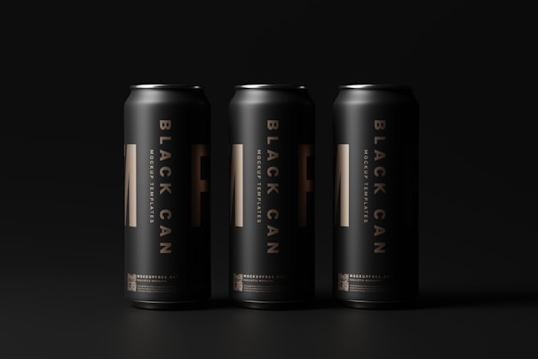 Three tall, sleek black cans are arranged side by side against a dark background. Each can features bold vertical lettering and subtle golden details, creating a modern and elegant aesthetic.