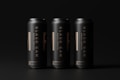 Three tall, sleek black cans are arranged side by side against a dark background. Each can features bold vertical lettering and subtle golden details, creating a modern and elegant aesthetic.