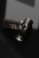 Two sleek, matte black cans with a minimalist design lie on a glossy black surface. The cans are labeled 'Black Can' in subtle lighting, enhancing the elegance of the presentation. The lighting creates soft reflections and shadows, adding to the modern aesthetic.