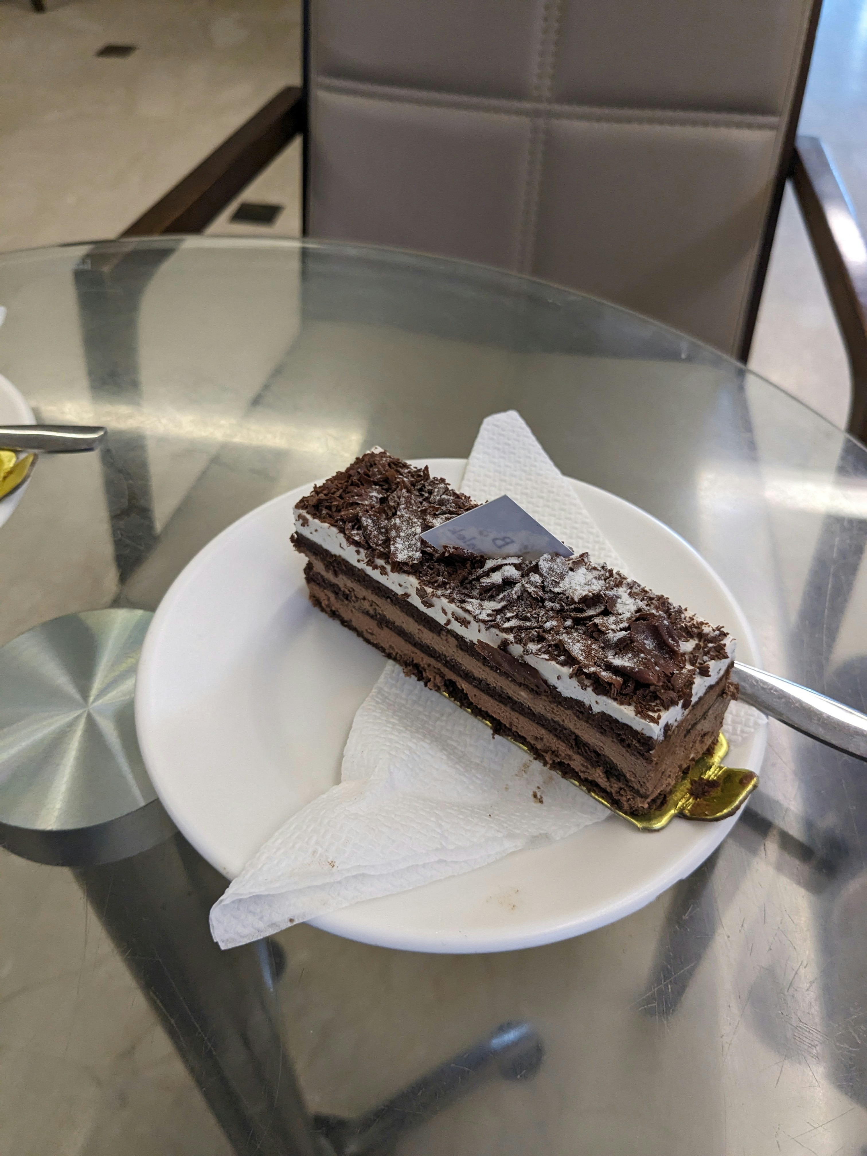 Chocolate layer cake slice with dark frosting on white plate
