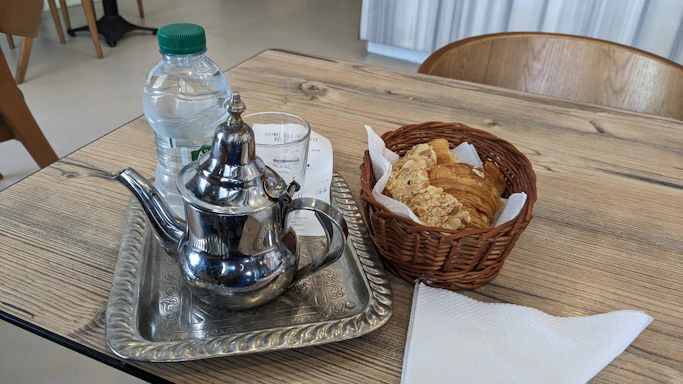 A rustic wooden table displaying a variety of freshly baked breads, muffins, and steaming cups of herbal tea.