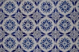 Intricate blue and white ceramic tiles featuring repetitive floral and geometric patterns. The design showcases a circular floral motif surrounded by ornate, symmetrical shapes, creating a harmonious and classic aesthetic.