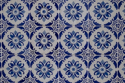 Intricate blue and white ceramic tiles featuring repetitive floral and geometric patterns. The design showcases a circular floral motif surrounded by ornate, symmetrical shapes, creating a harmonious and classic aesthetic.