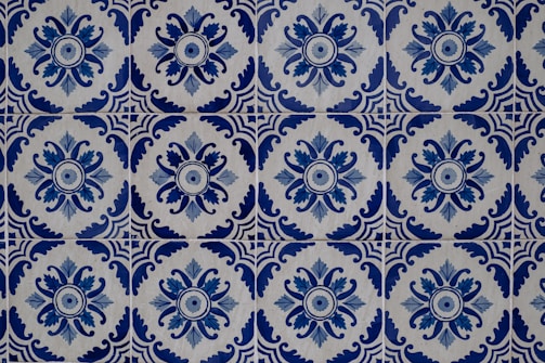 Intricate blue and white ceramic tiles featuring repetitive floral and geometric patterns. The design showcases a circular floral motif surrounded by ornate, symmetrical shapes, creating a harmonious and classic aesthetic.