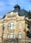 A historic building with an ornate architectural style. The structure features a mix of brick and stone with large windows and decorative elements near the roof. It has a prominent section labeled 'Biblioteca Universitară' and a dark slate roof with a small tower.