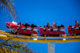 A lively family enjoying a roller coaster at a bustling theme park under bright blue skies.