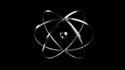 A metallic representation of an atom, with a central nucleus and orbiting paths for electrons, set against a black background.