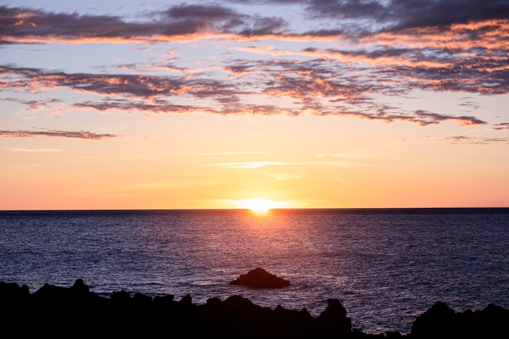 the sun is setting over the ocean on a cloudy day