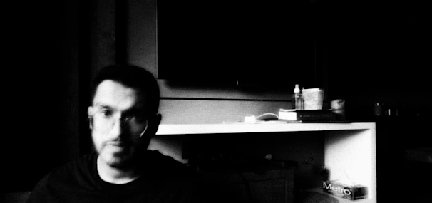 A black-and-white still from a short film showing a thoughtful man in a dimly lit room.