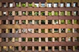 Bricks arranged in an interlocking pattern, creating a grid-like structure. The background shows greenery, with leaves and possibly trees visible through the gaps.