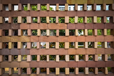 Bricks arranged in an interlocking pattern, creating a grid-like structure. The background shows greenery, with leaves and possibly trees visible through the gaps.