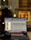 A laptop displaying an audio editing or digital audio workstation (DAW) software with various tracks and controls on the screen. A pair of headphones rests beside the laptop, suggesting an audio production or mixing environment. The blurred background indicates an indoor setting, possibly near a window, with warm lighting.