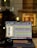 A laptop displaying an audio editing or digital audio workstation (DAW) software with various tracks and controls on the screen. A pair of headphones rests beside the laptop, suggesting an audio production or mixing environment. The blurred background indicates an indoor setting, possibly near a window, with warm lighting.
