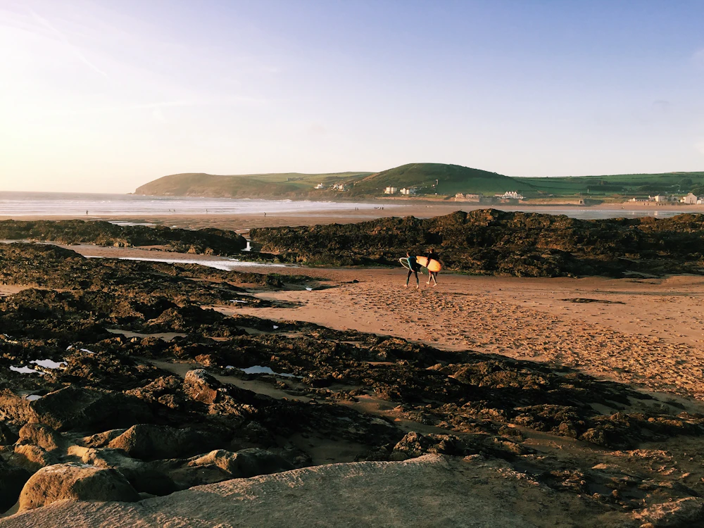 A surfer holding a board on a rocky beach