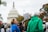 A crowd of people gather outside a government building, holding signs. The U.S. Capitol building is visible in the background. One prominent sign reads 'STOP WEAPONIZING OUR GRIEF.' The group appears to be part of a protest or rally, with individuals wearing varied clothing including a bright green jacket and a blue shirt.