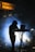 A person is silhouetted against bright stage lights while standing behind a music mixing console. Fog or smoke creates a dramatic effect, and a sign above reads 'FRIENDSHIP MOMENTS.' The setting suggests a musical performance or DJ event.