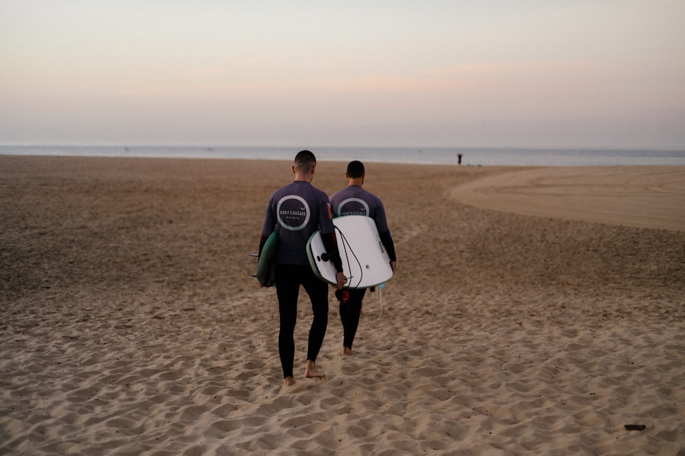 two people walking on a beach carrying surfboards