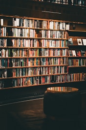 A cozy wooden bookshelf filled with physical books, bathed in warm natural light.