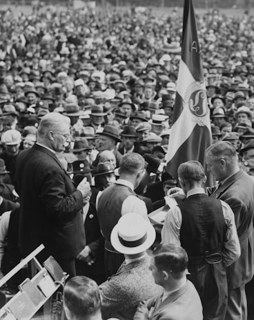 Black and white photo of a 1920s press conference with reporters crowded around a podium.