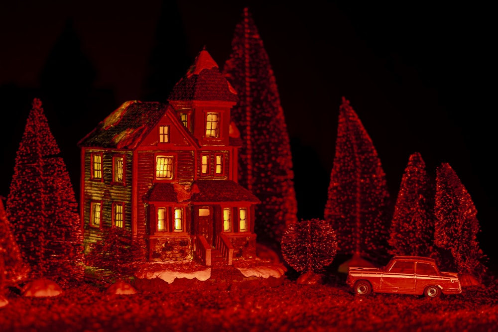 a lighted house with trees and a car in front of it